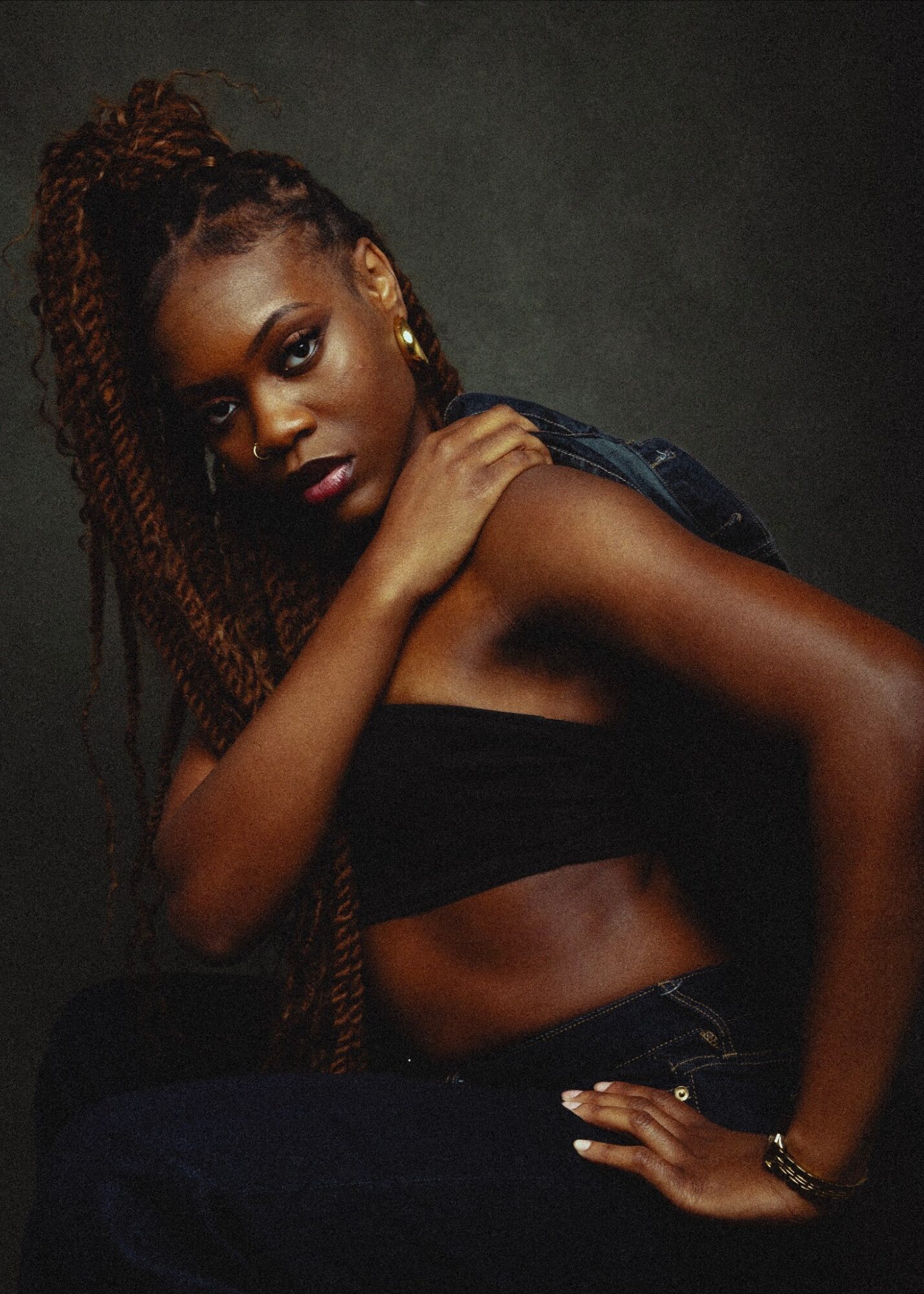 Young woman with long braided hair, wearing a black top, posing against a dark background.