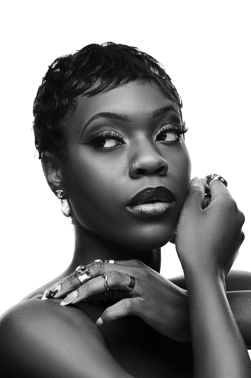 Portrait of a woman with short hair, looking sideways, with hand near face, wearing rings, in black and white.