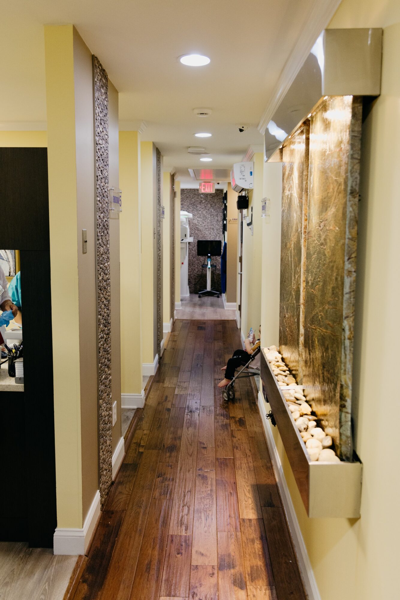 Long hallway with yellow walls, wooden floor, and decorative wall features, leading to a door at the end.