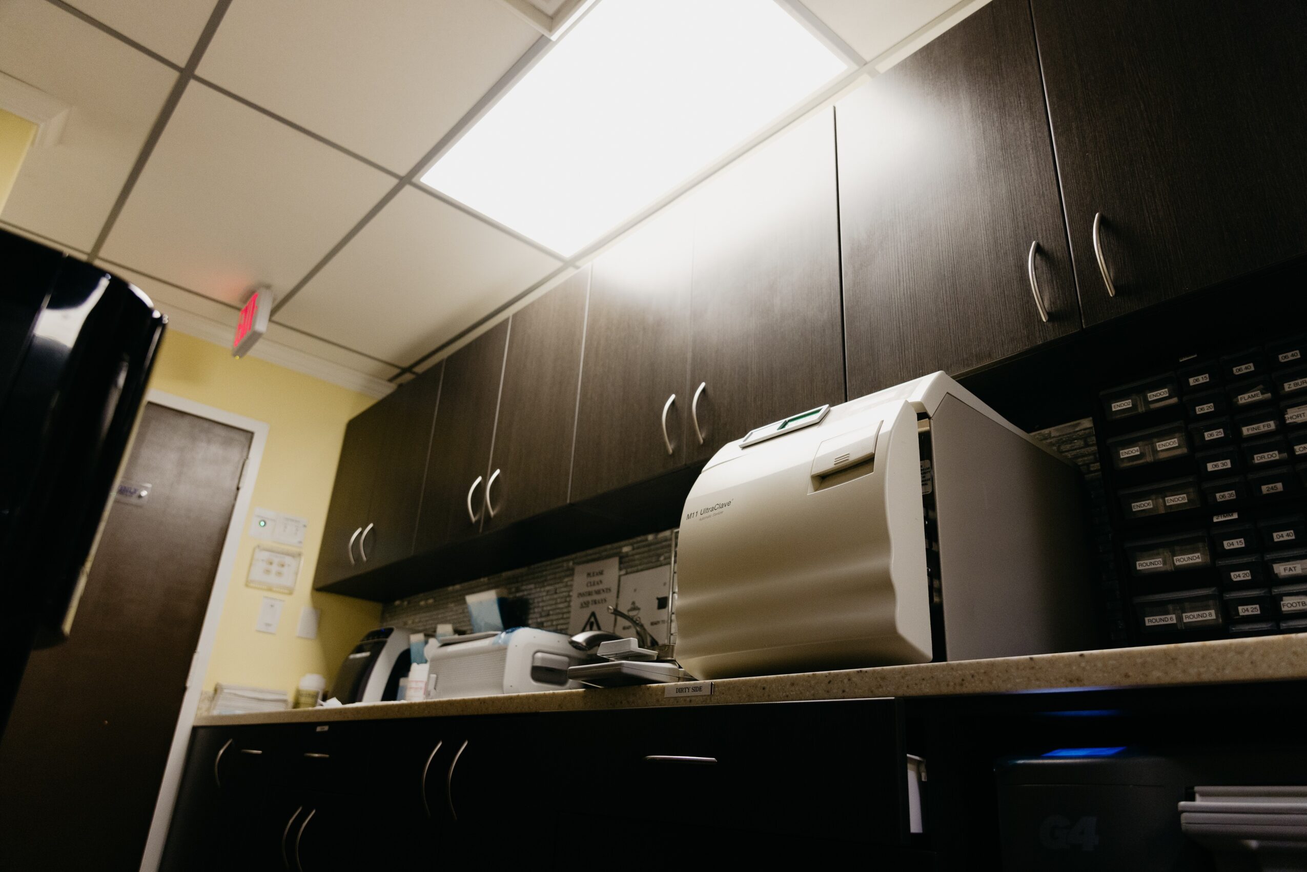 Kitchen counter with dark cabinets, a white paper shredder, and various office supplies, viewed from a low angle.