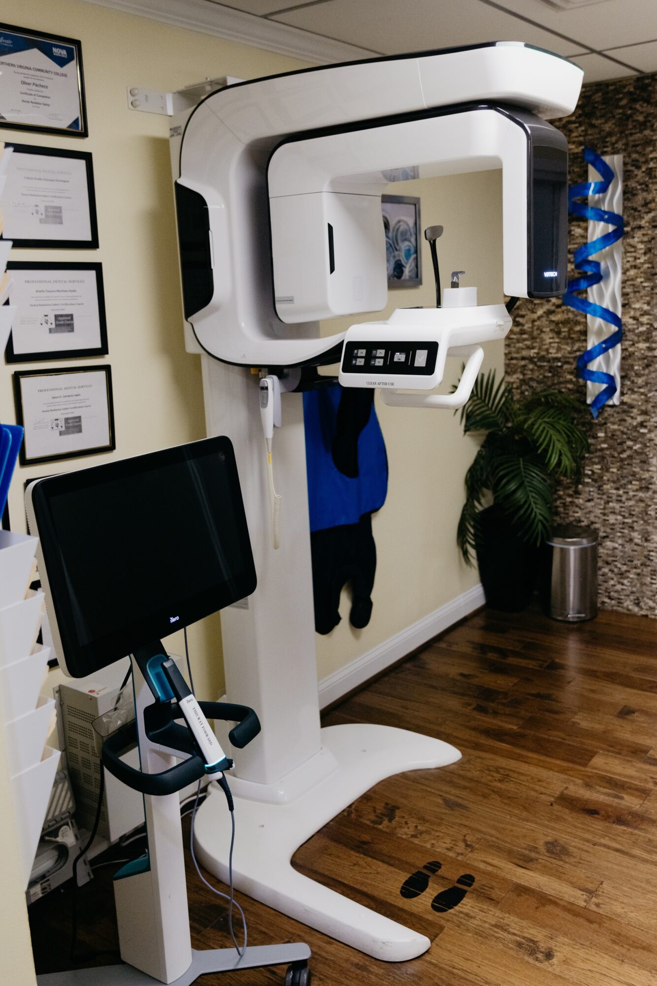 Medical imaging machine with control panel and monitor in a room with certificates and plants.