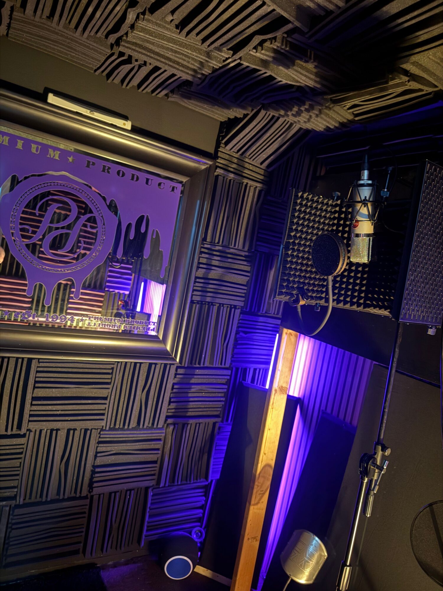 Recording studio with soundproofed walls, a mirror, and purple lighting, showing equipment and acoustic panels.