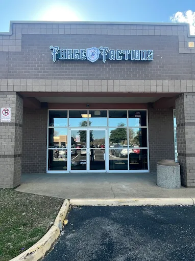 Front entrance of a building with glass doors and a sign reading 'Torgo Tactius' above, reflecting parking lot and trees.