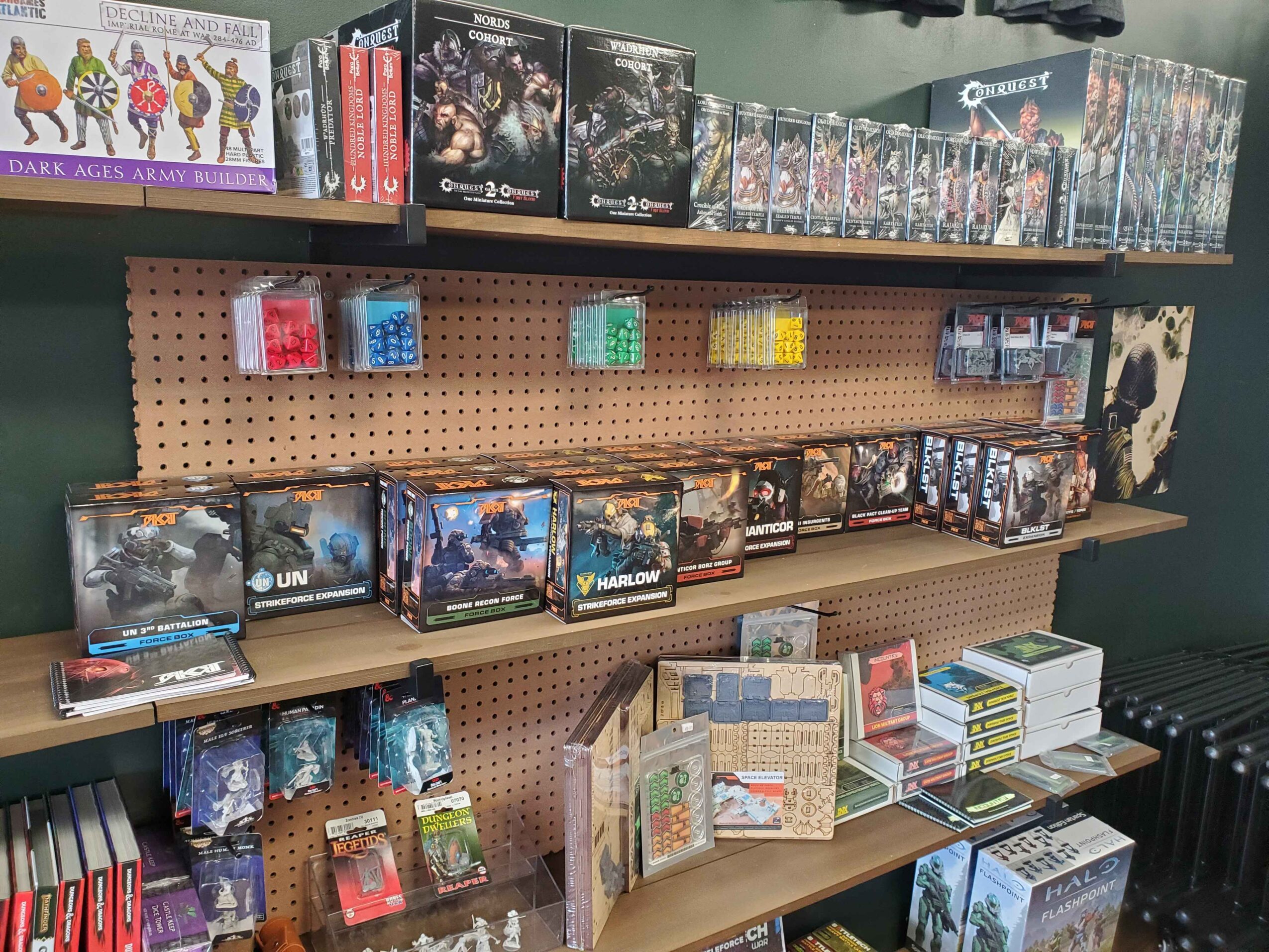 Books and board games on shelves, with various game boxes and card packs visible, organized on a pegboard and wooden shelves.