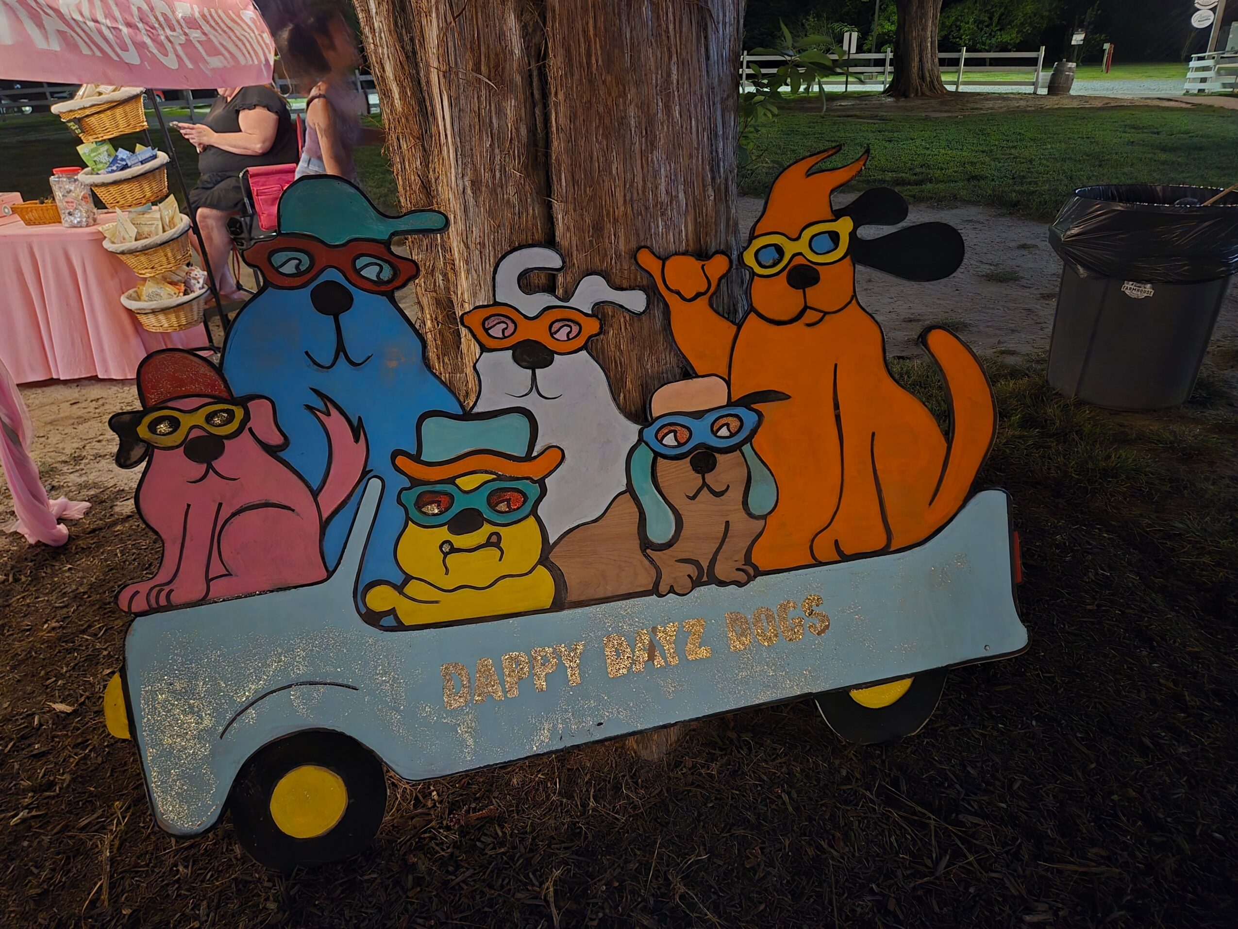 Colorful cutout of dogs wearing sunglasses in a cart with a banner reading 'Happy Dog Day!'.