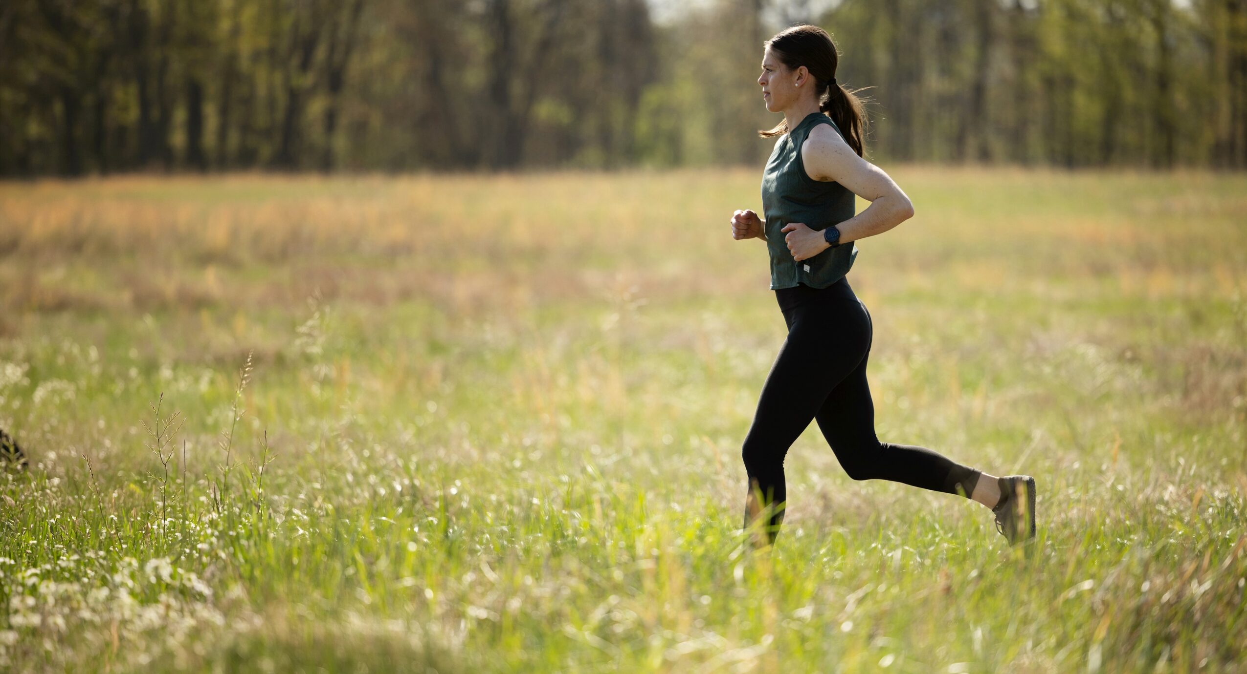 Person running in a grassy field with trees in the background.