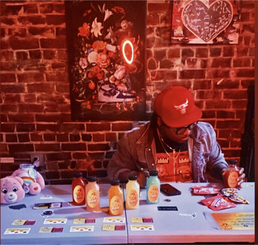Person wearing a red cap and jacket sitting at a table with bottles and cards, brick wall background, Valentine's Day decorations.