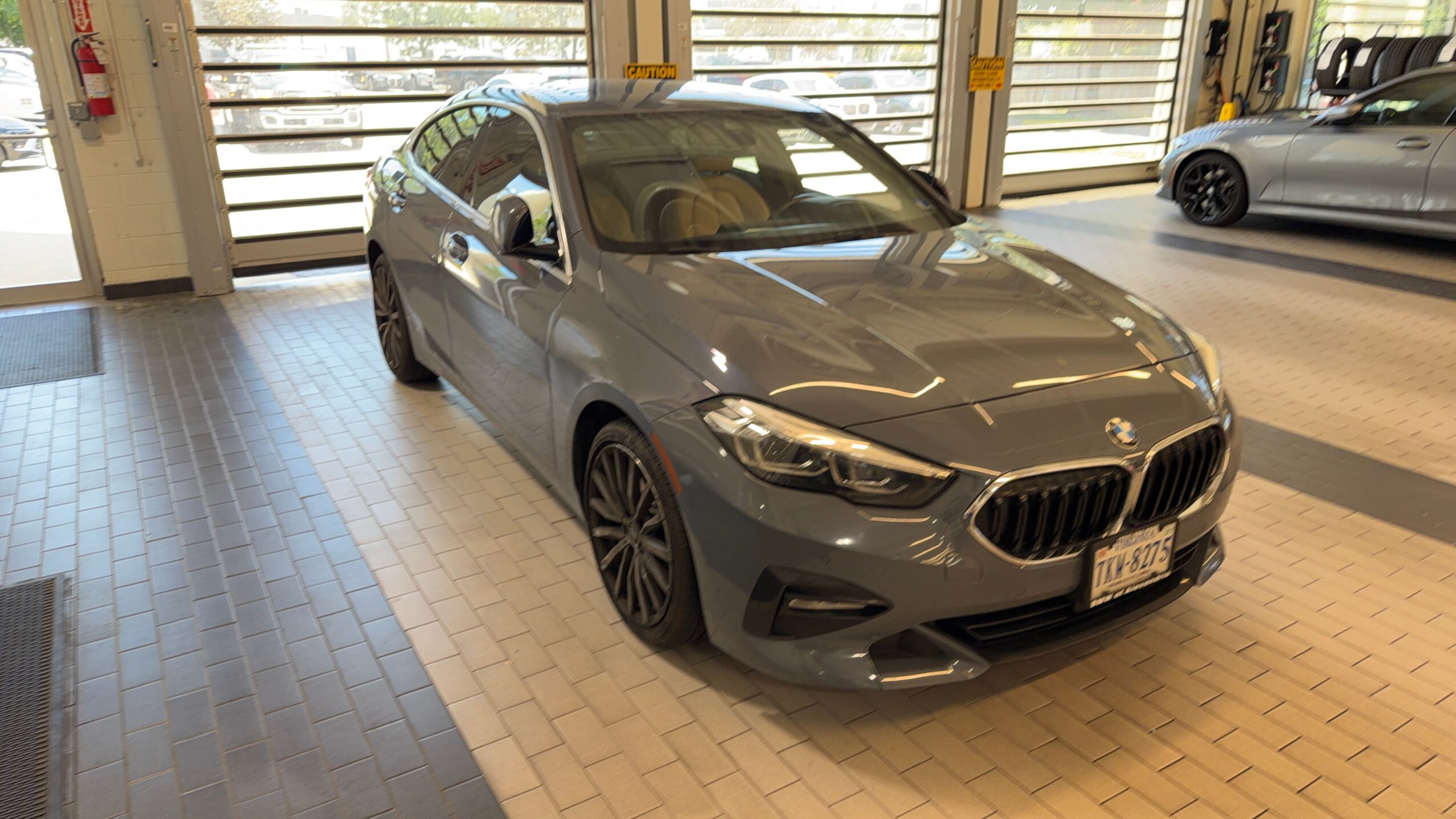 Gray BMW sedan parked indoors with garage doors in background, front view, well-lit environment.