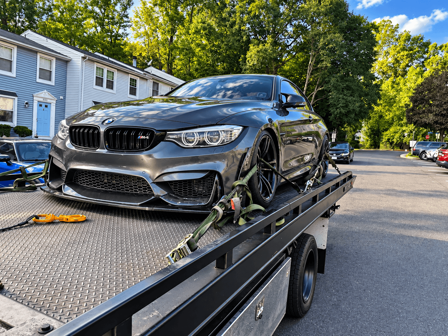 Black sports car on a flatbed tow truck in a parking lot with trees and buildings in the background.