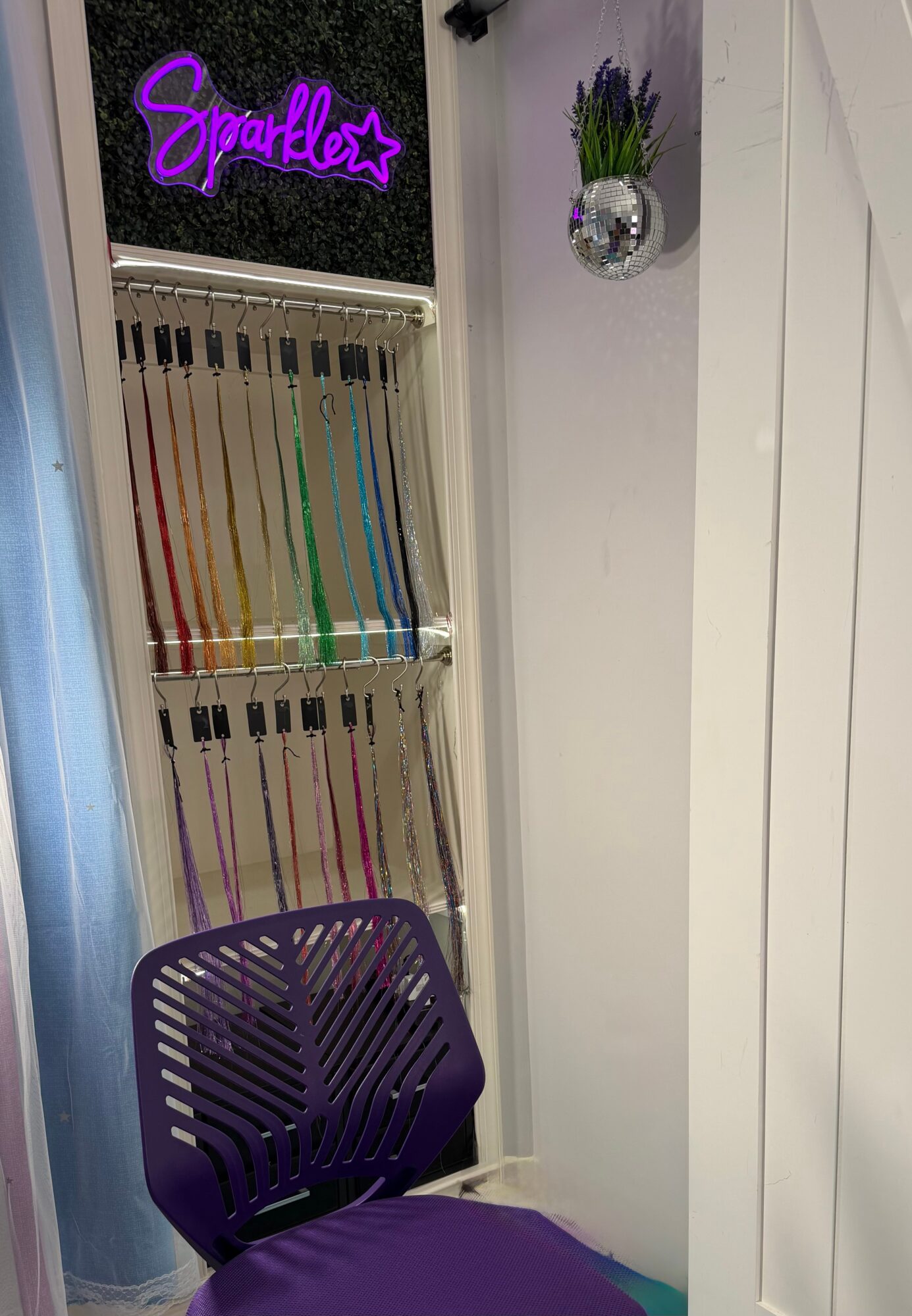 Purple chair in front of a white wall with a small potted plant and a neon sign reading 'Sparkle' in purple.