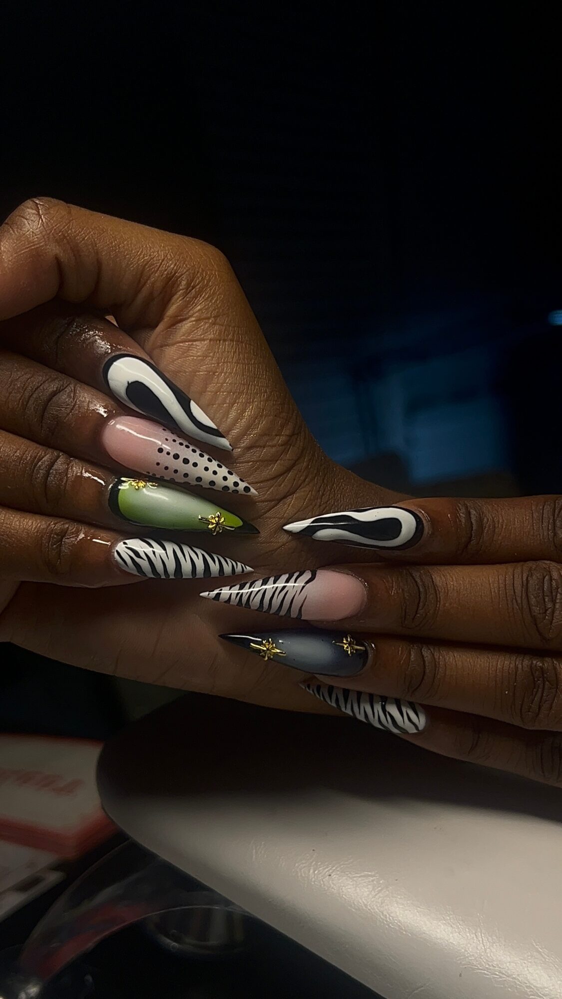 Close-up of hands with colorful, patterned nails resting on a white surface, dark background, and reflections visible.