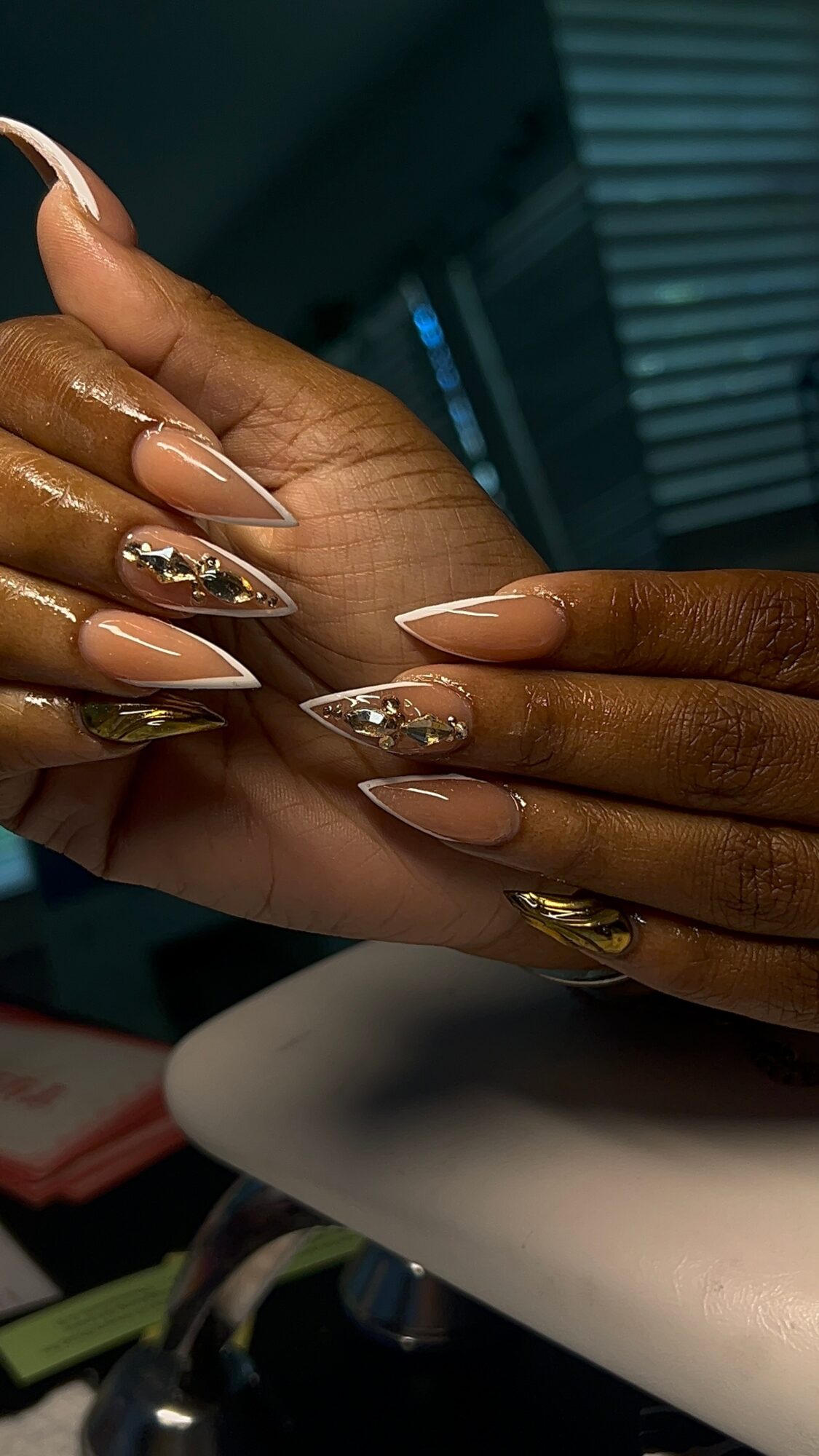 Close-up of hands with manicured nails, some decorated with gold and silver accents, against a dark background.