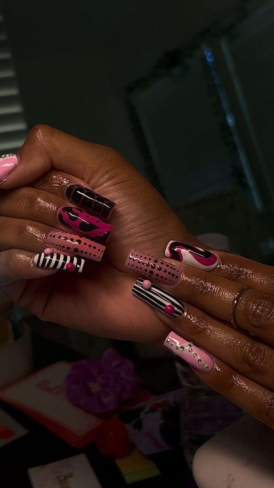 Close-up of hands with decorated nails, featuring pink, black, and white patterns, in a dimly lit room.