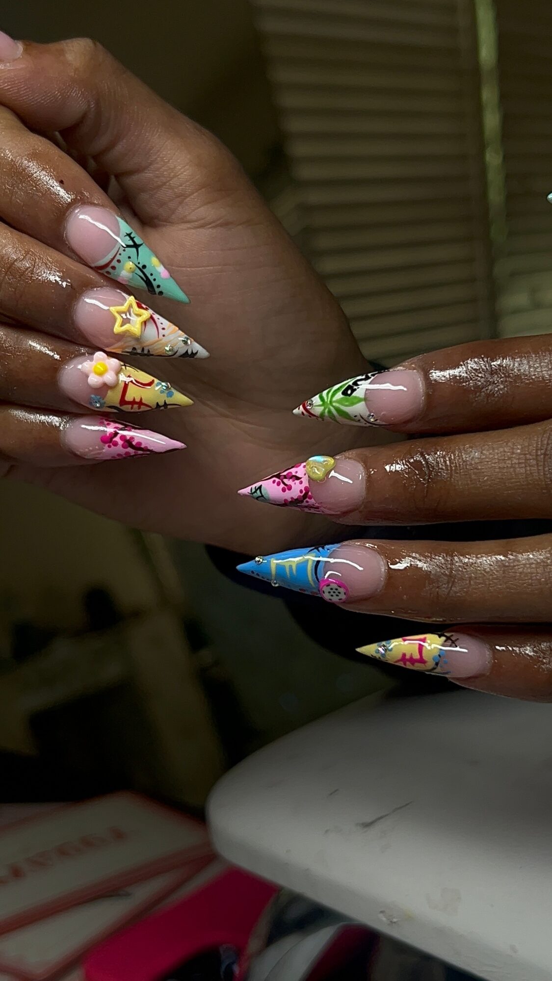 Hands with colorful, decorated nails, some with star and cartoon character designs, held together, background blurred.