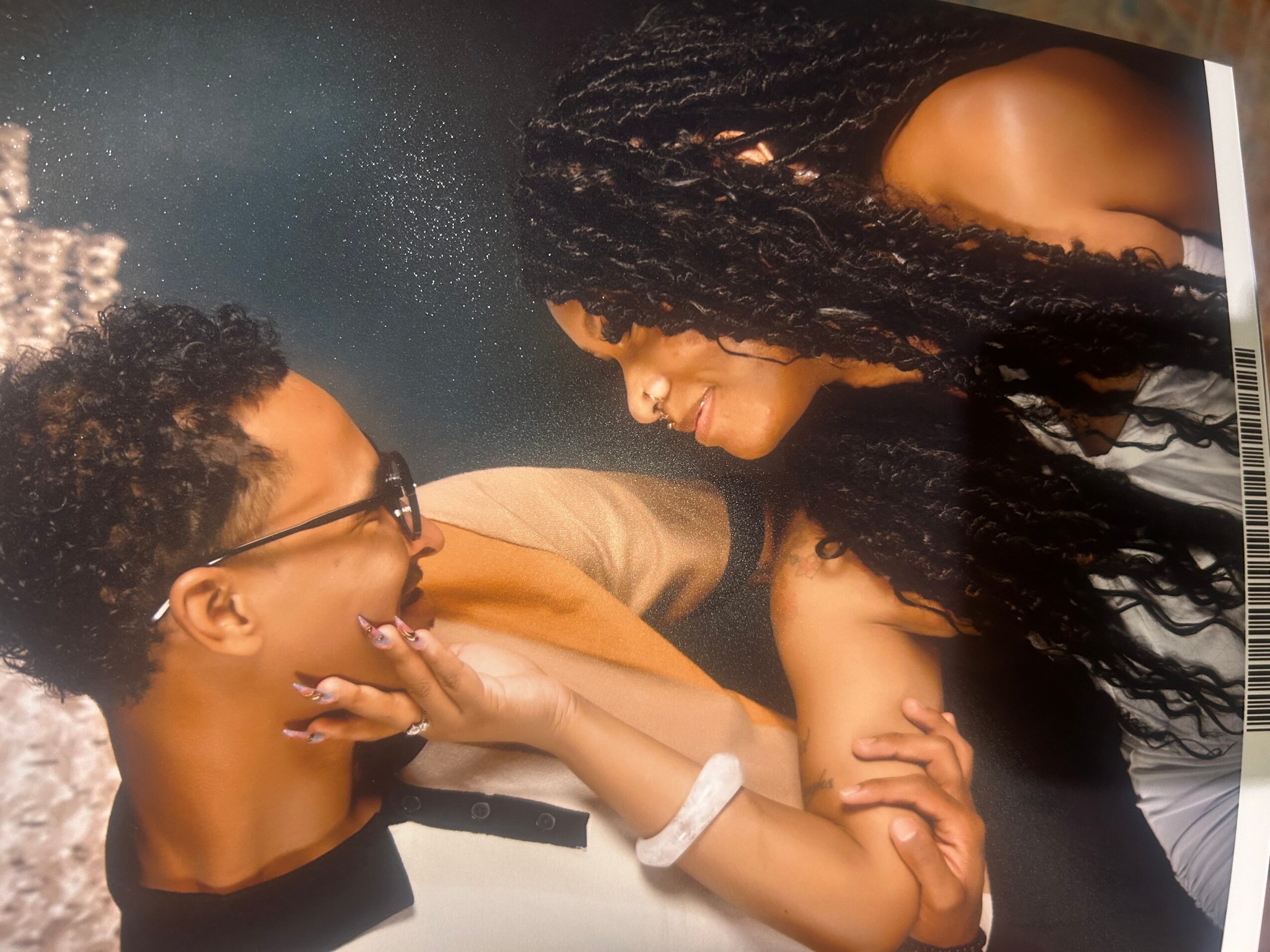 Two women face each other closely, one touching the other's chin, in a dimly lit setting.