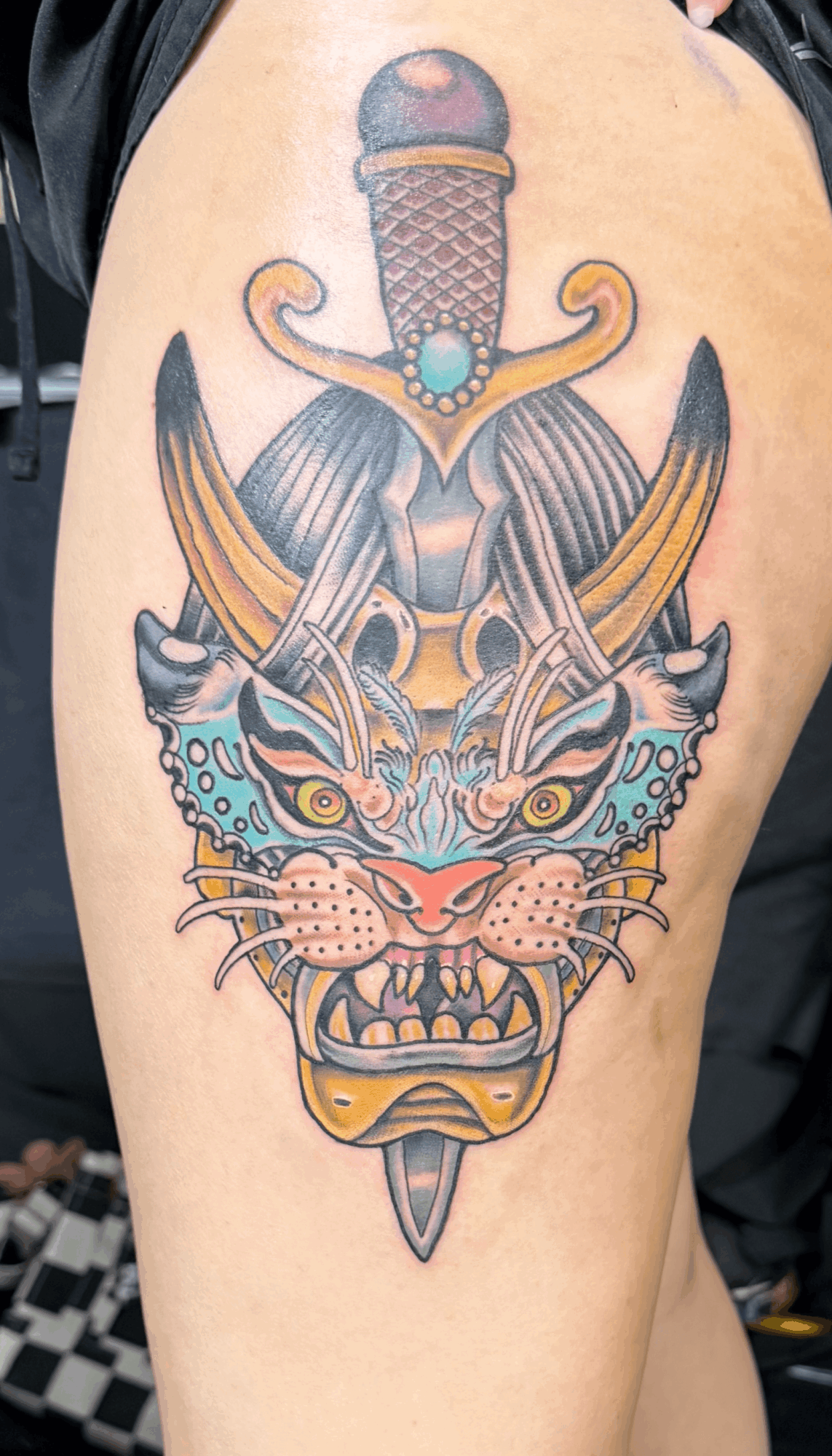 Tattoo of a fierce tiger's face with a sword and dagger crossed behind it, colorful and detailed.