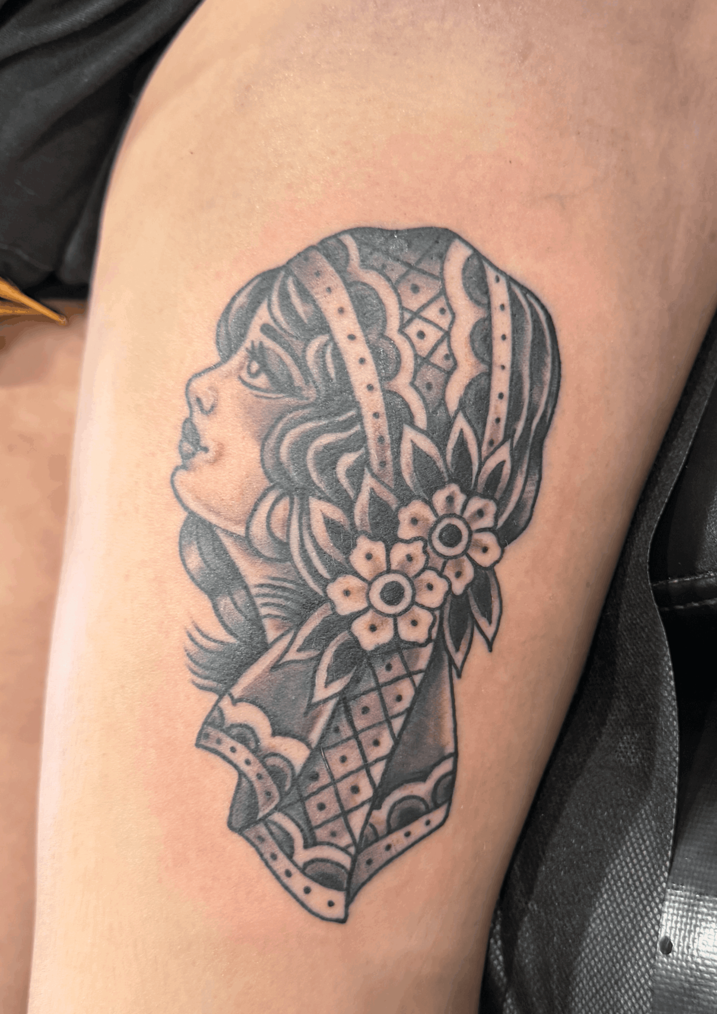 Black and gray tattoo of a woman's profile with floral and decorative patterns on her head, on upper arm.