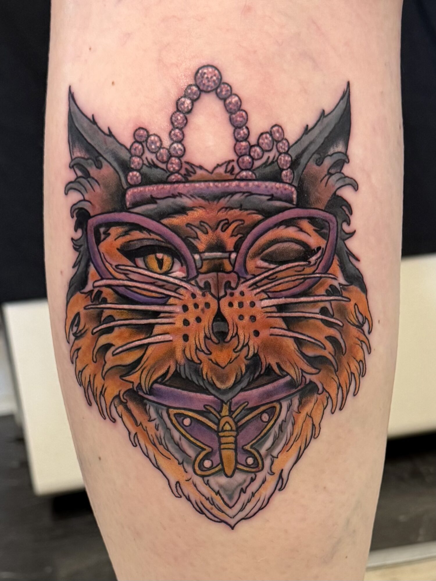 Colorful tiger face tattoo with glasses, a crown, and a butterfly, featuring detailed line work and shading.