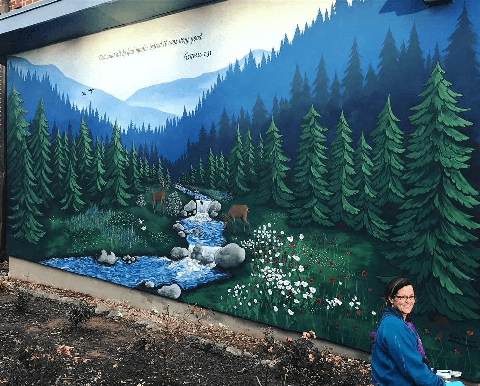 Colorful mural of a mountain landscape with trees, a river, rocks, and a person in the foreground.