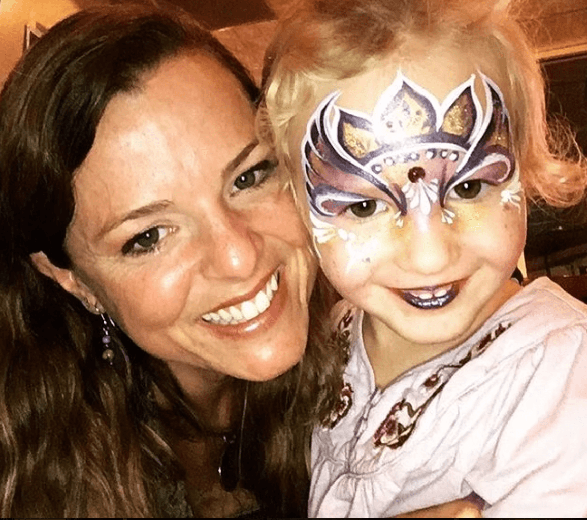 Woman and child with face paint, smiling, close-up photo, warm indoor lighting.