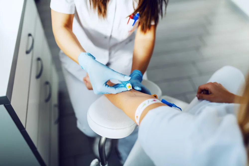 Healthcare professional drawing blood from a patient's arm in a clinical setting.