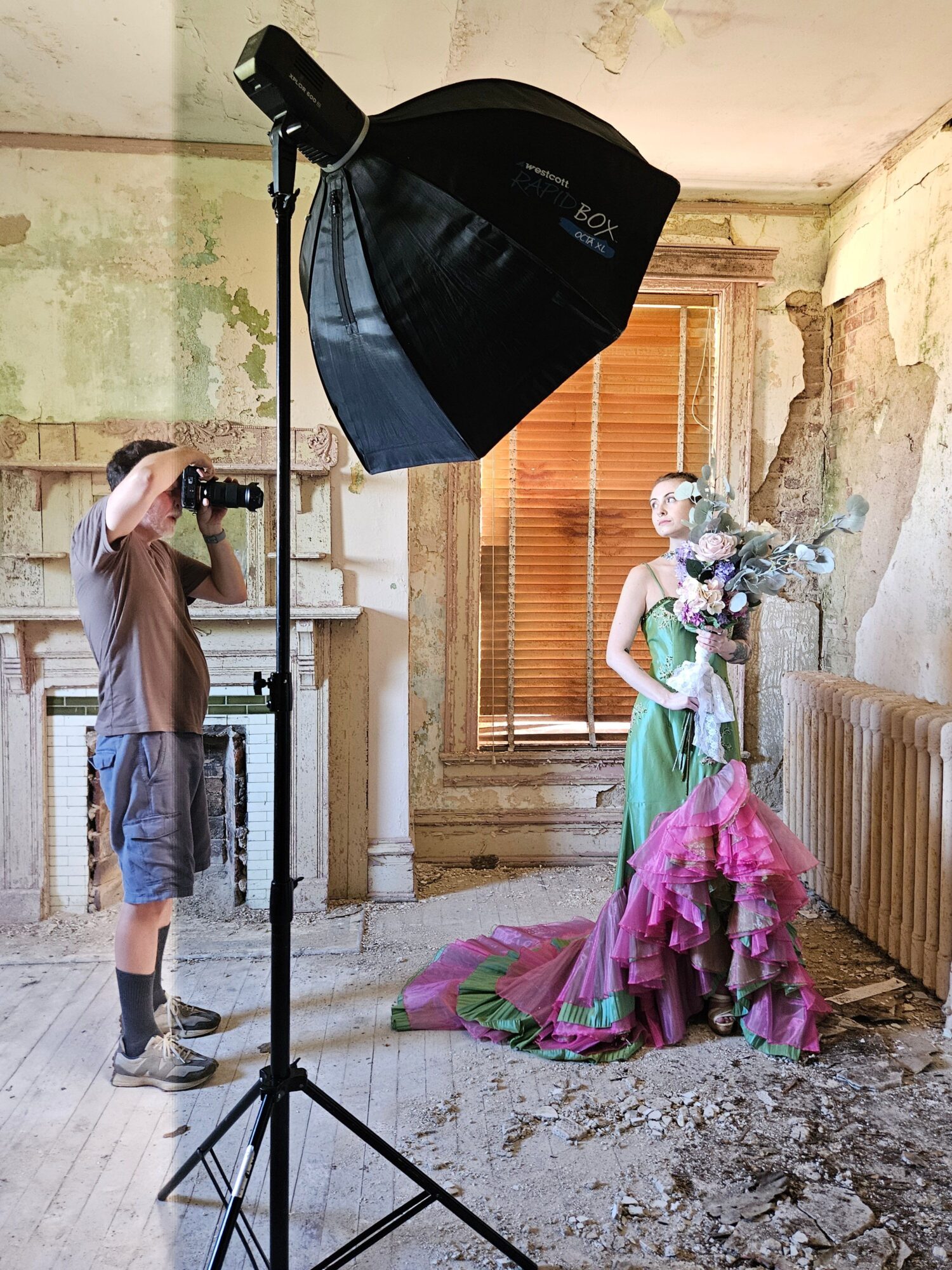 Person taking a photo of a statue in a room with peeling walls and wooden window shutters, using a camera and softbox light.