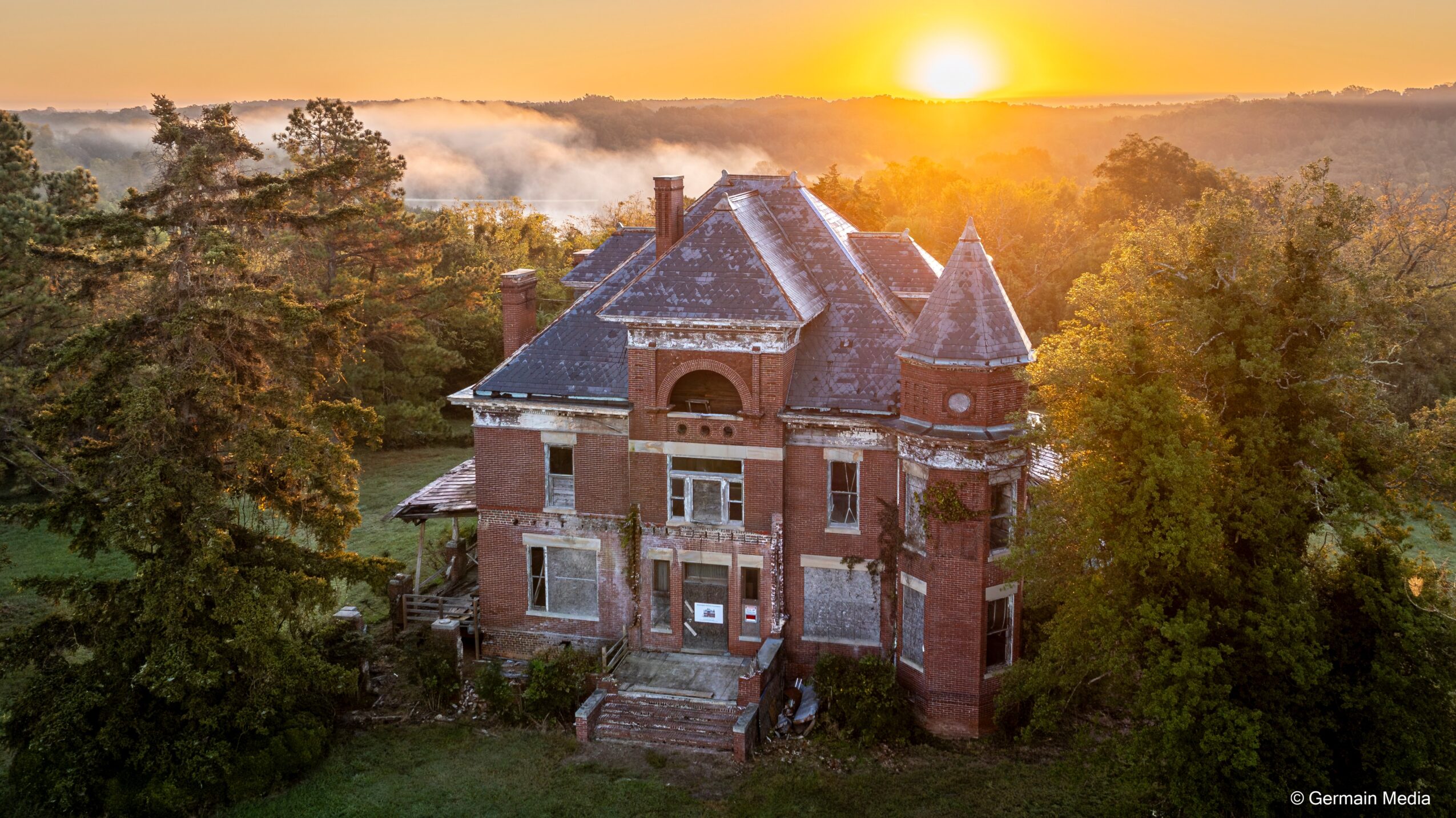 Sunset over a large brick castle with turrets, surrounded by trees and greenery.