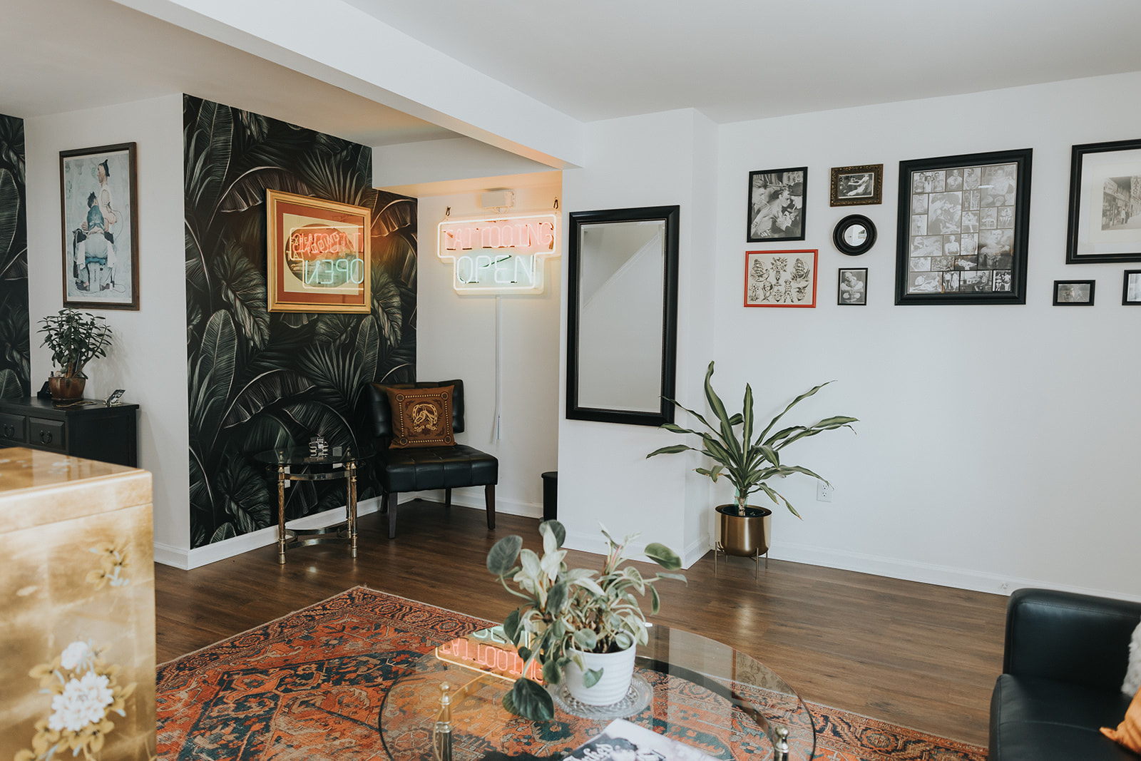 Living room with white walls, framed pictures, a large mirror, a potted plant, and a glass table with a plant in a white pot.
