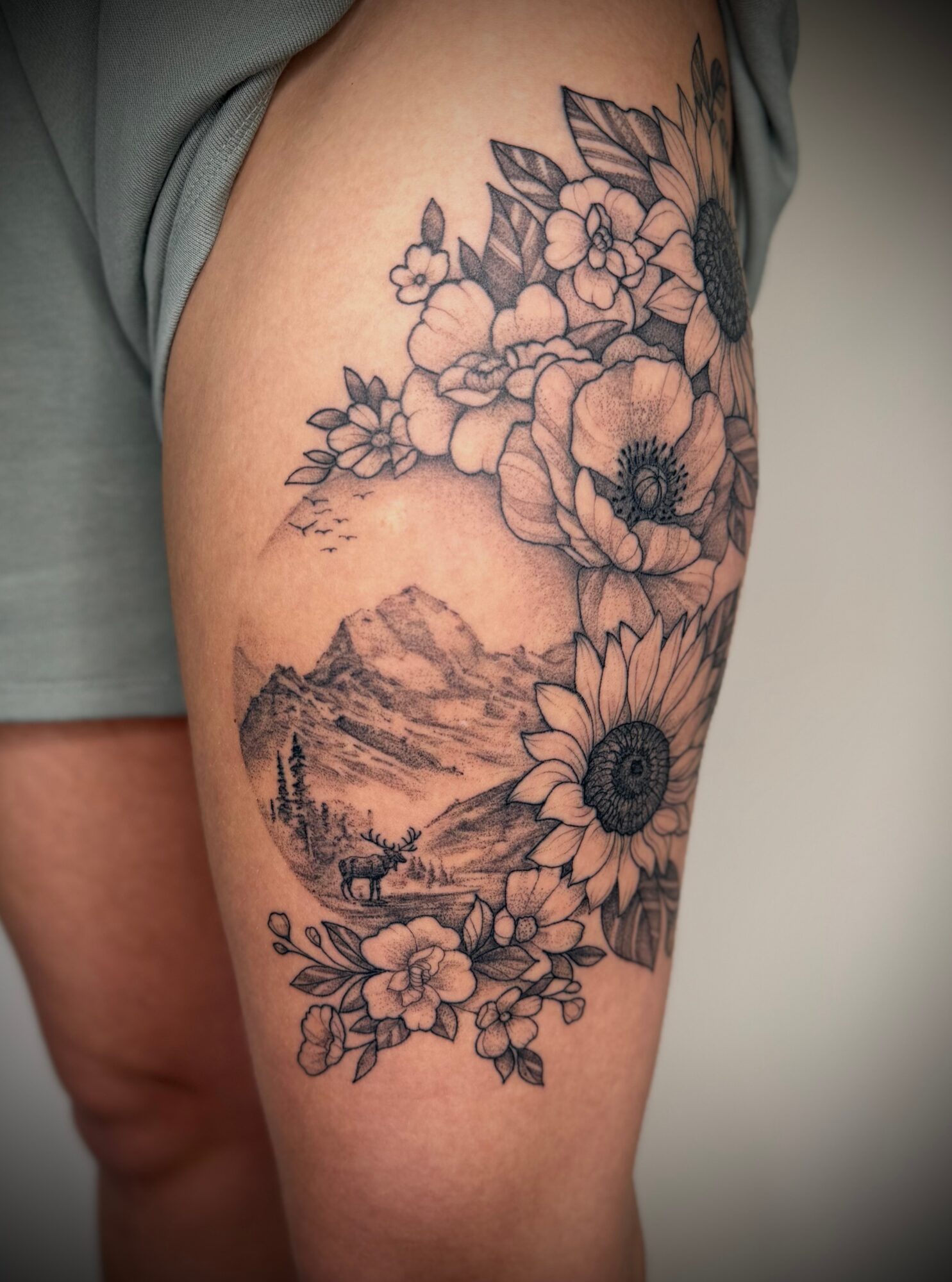 Tattoo of flowers and a mountain landscape on person's upper arm.