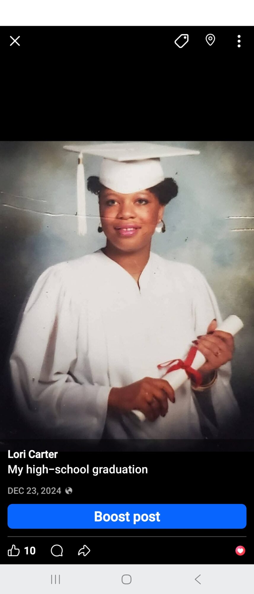 Woman in graduation cap and gown holding diploma, smiling, against a plain background.