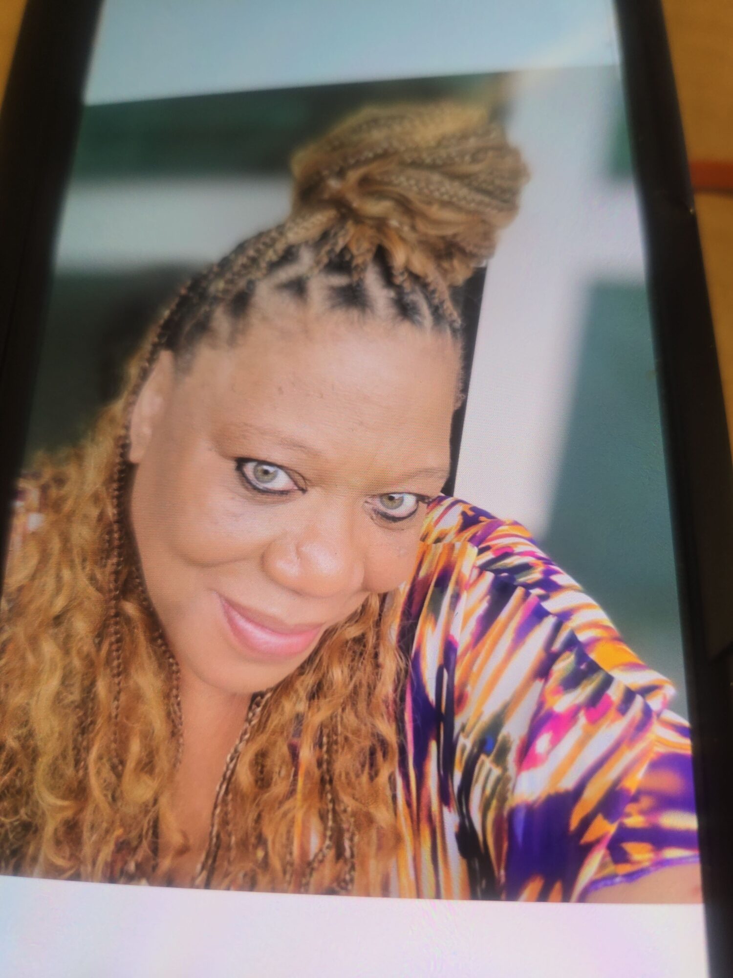 Woman with braided hair and colorful top, smiling, looking upward, with light-colored background.