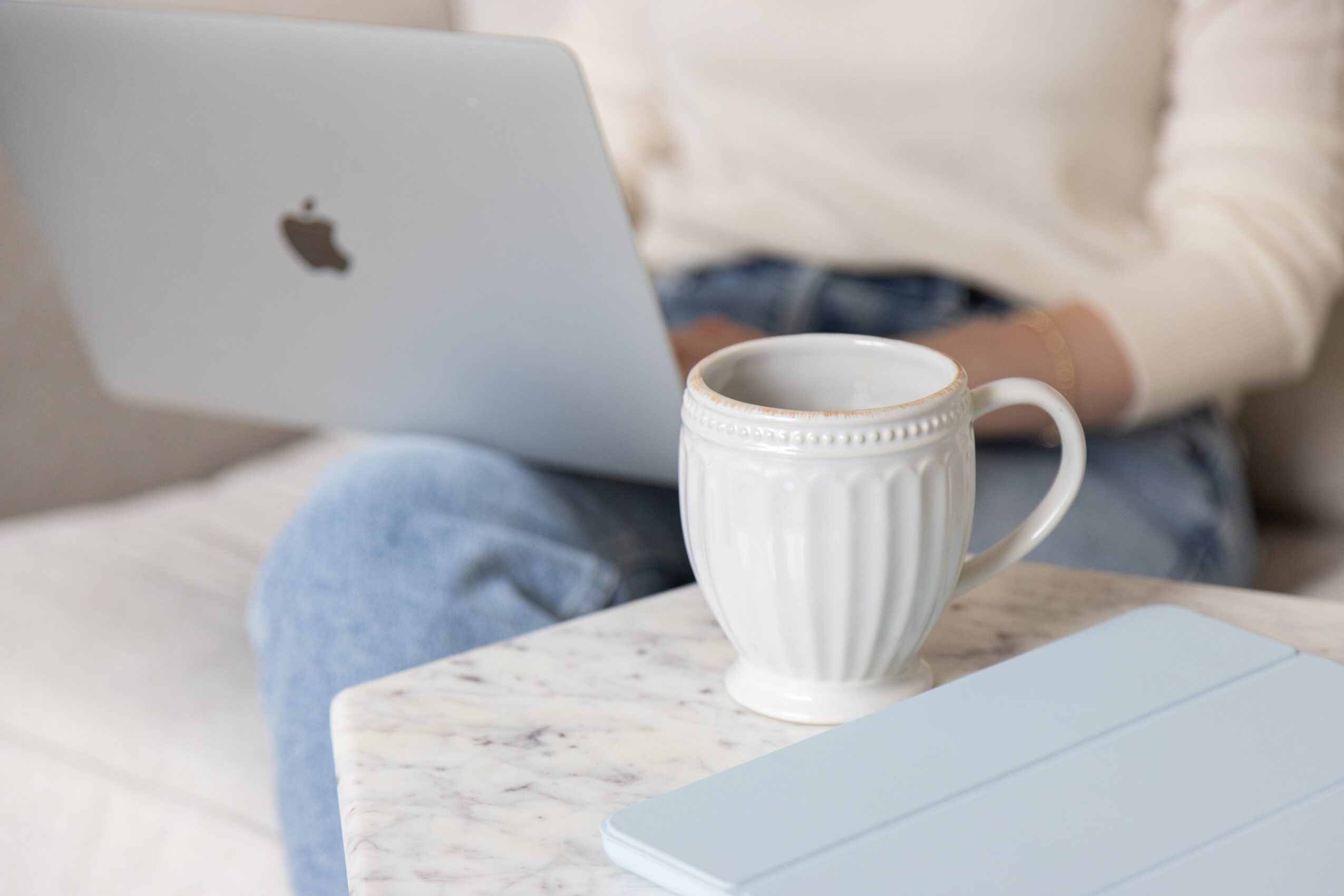 Person sitting on a couch with a laptop and a white mug on a marble table.