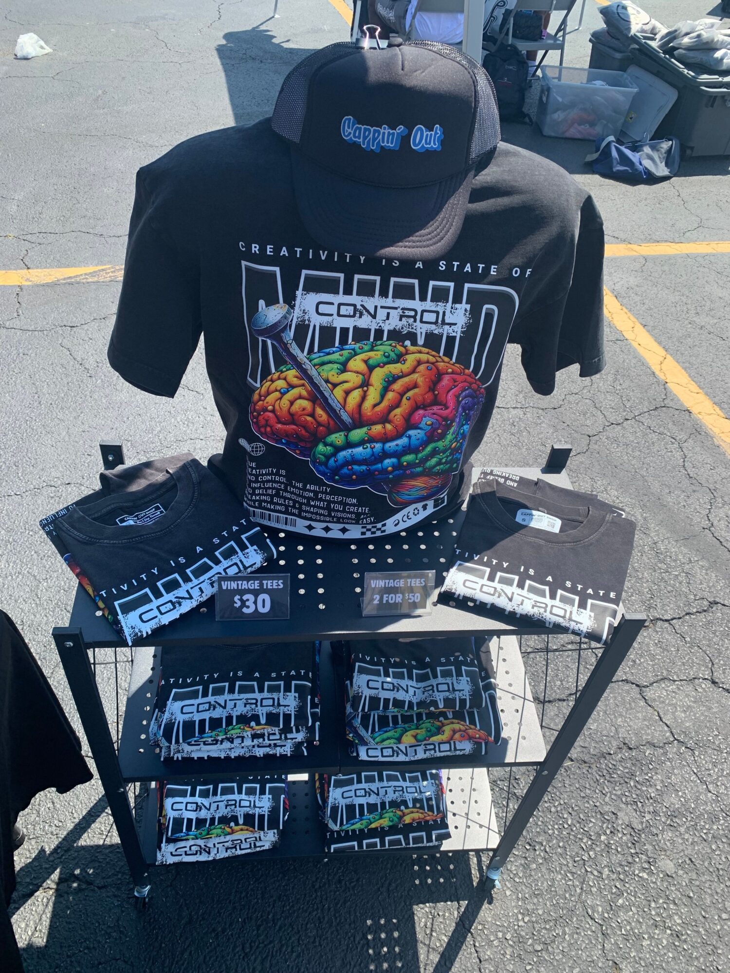 Display table with colorful brain illustration, black hoodie, and packs of products on a black metal rack outdoors.