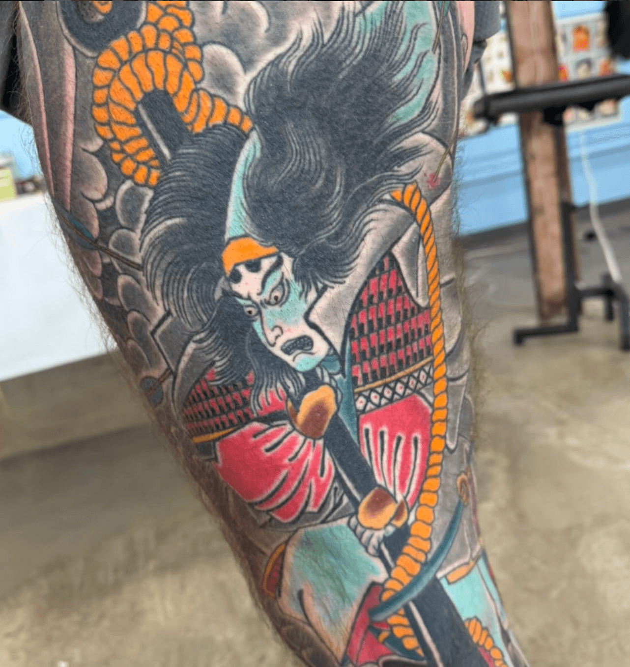 Tattoo of a woman with long black hair, red clothing, and a snake wrapped around her arm, on a person's arm.