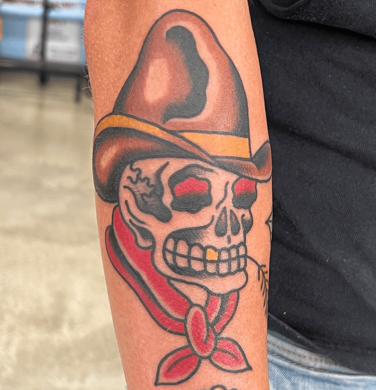 Skull wearing a cowboy hat with red eyes, bandana, and tongue sticking out, in traditional tattoo style.