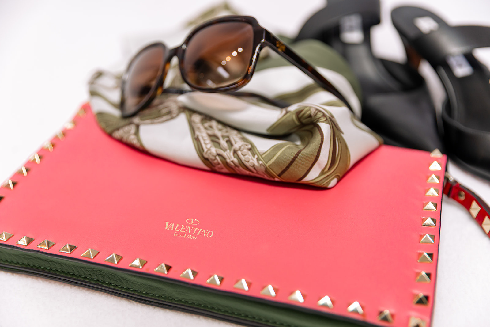 Sunglasses resting on a patterned scarf, placed on a red notebook with gold studs, with a black camera nearby.