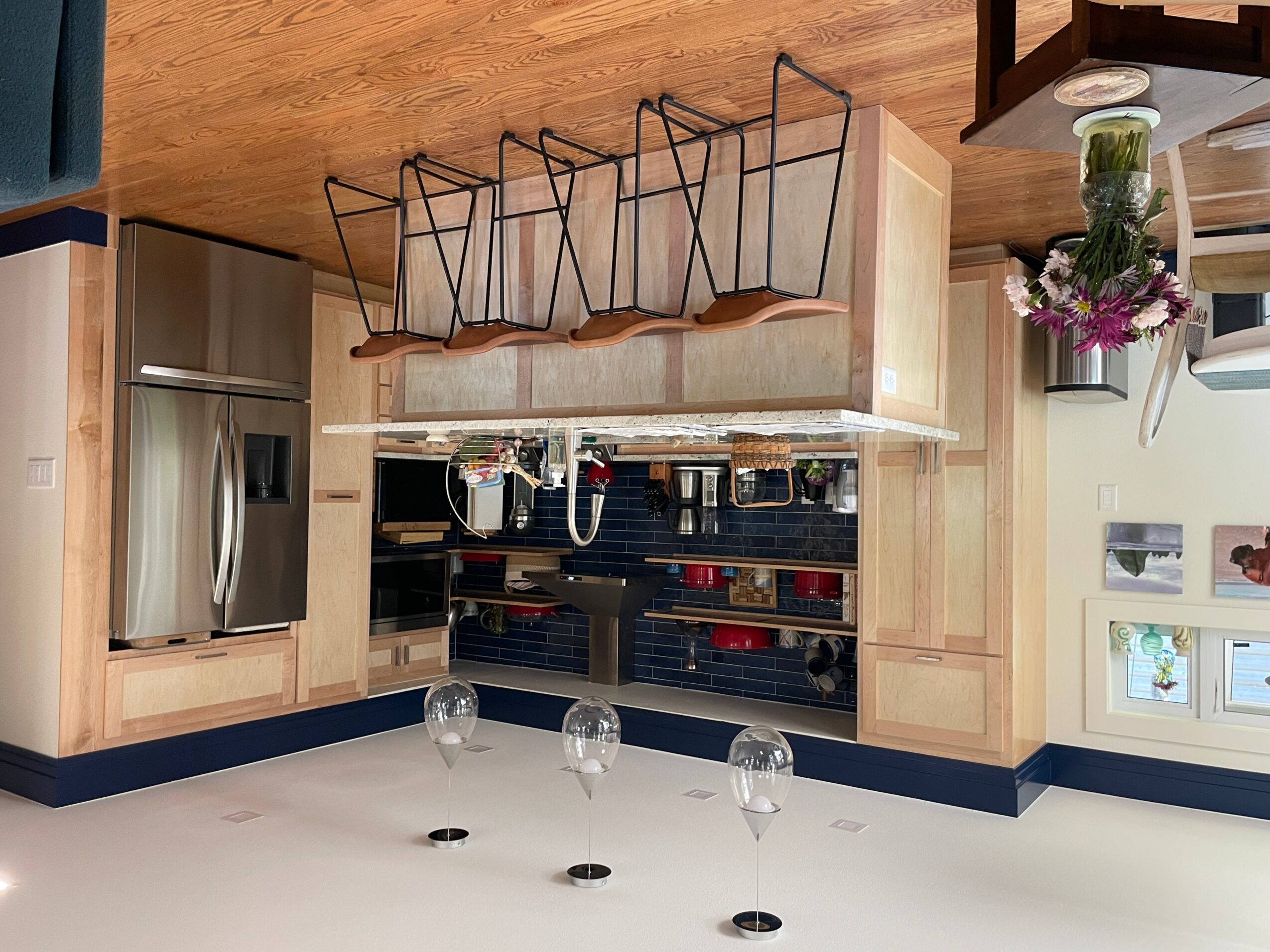 Kitchen with wooden cabinets, stainless steel refrigerator, and wine glasses on a white countertop, upside down view.