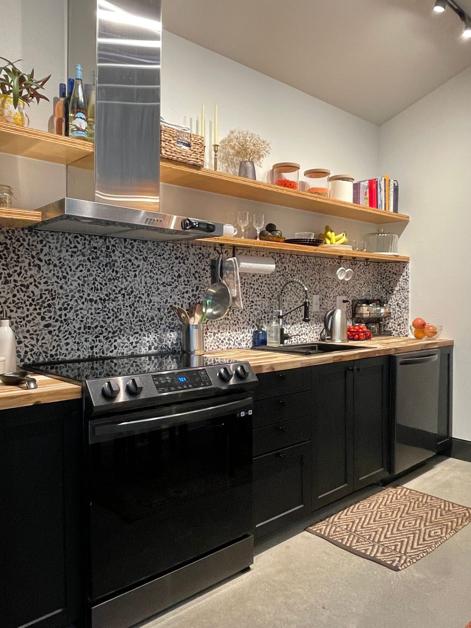 Kitchen counter with stove, black cabinets, and a granite countertop, with shelves and decorative items in the background.