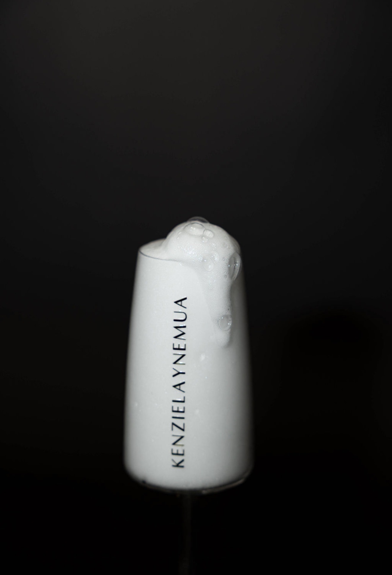 A white bottle with foam on top, standing against a black background, with text on the bottle.