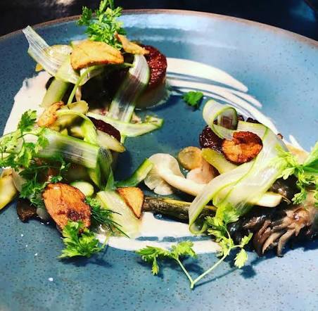 Plate with grilled vegetables, greens, and sauce, arranged artistically on a blue dish.