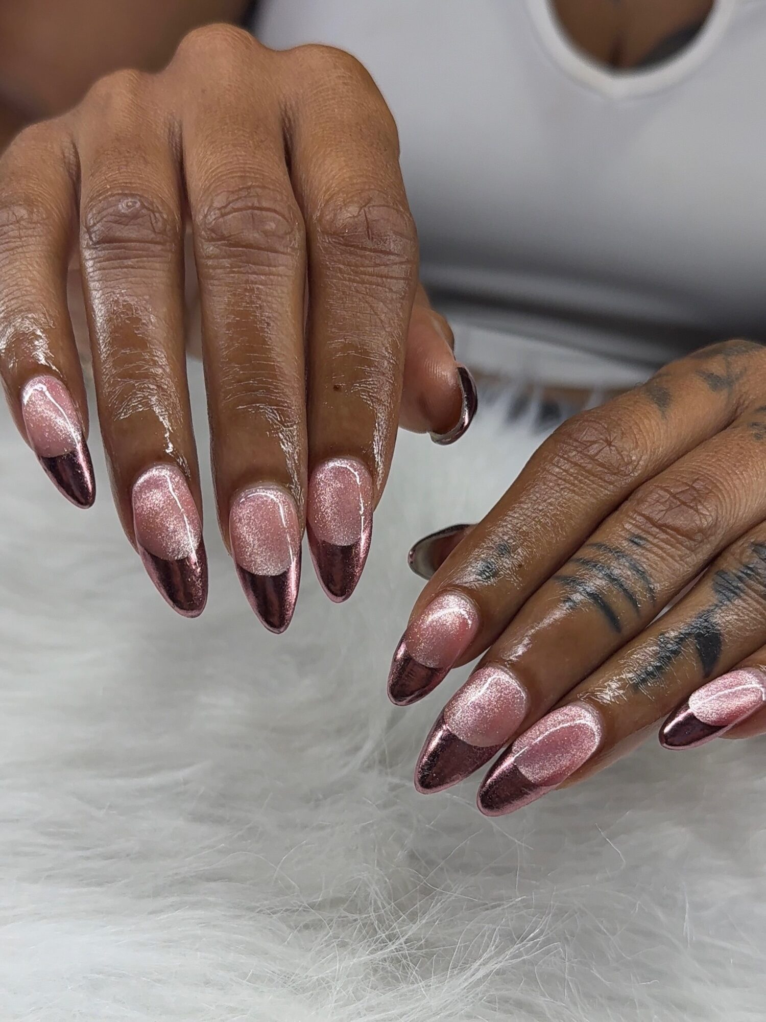 Close-up of hands with manicured nails resting on a soft surface, showing detailed nail art and tattoos.