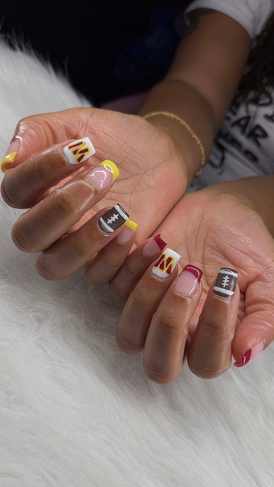 Close-up of hands with colorful, patterned nail art, resting on a white furry surface.