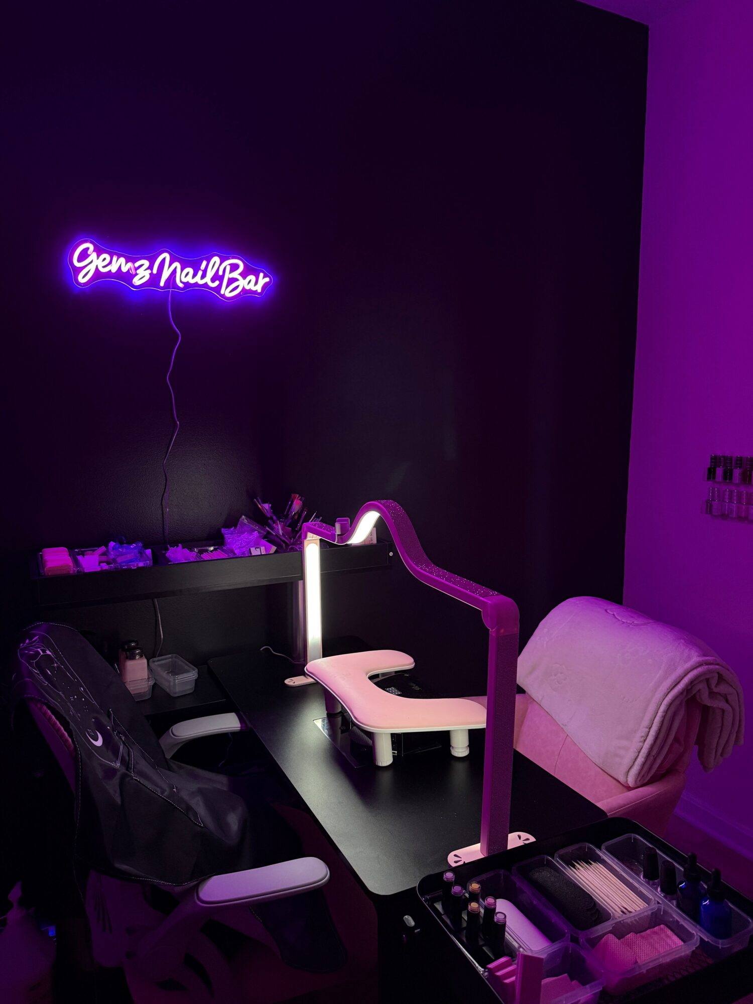 A dark room with purple lighting, a bed with a pink headboard, and a neon sign on the wall.