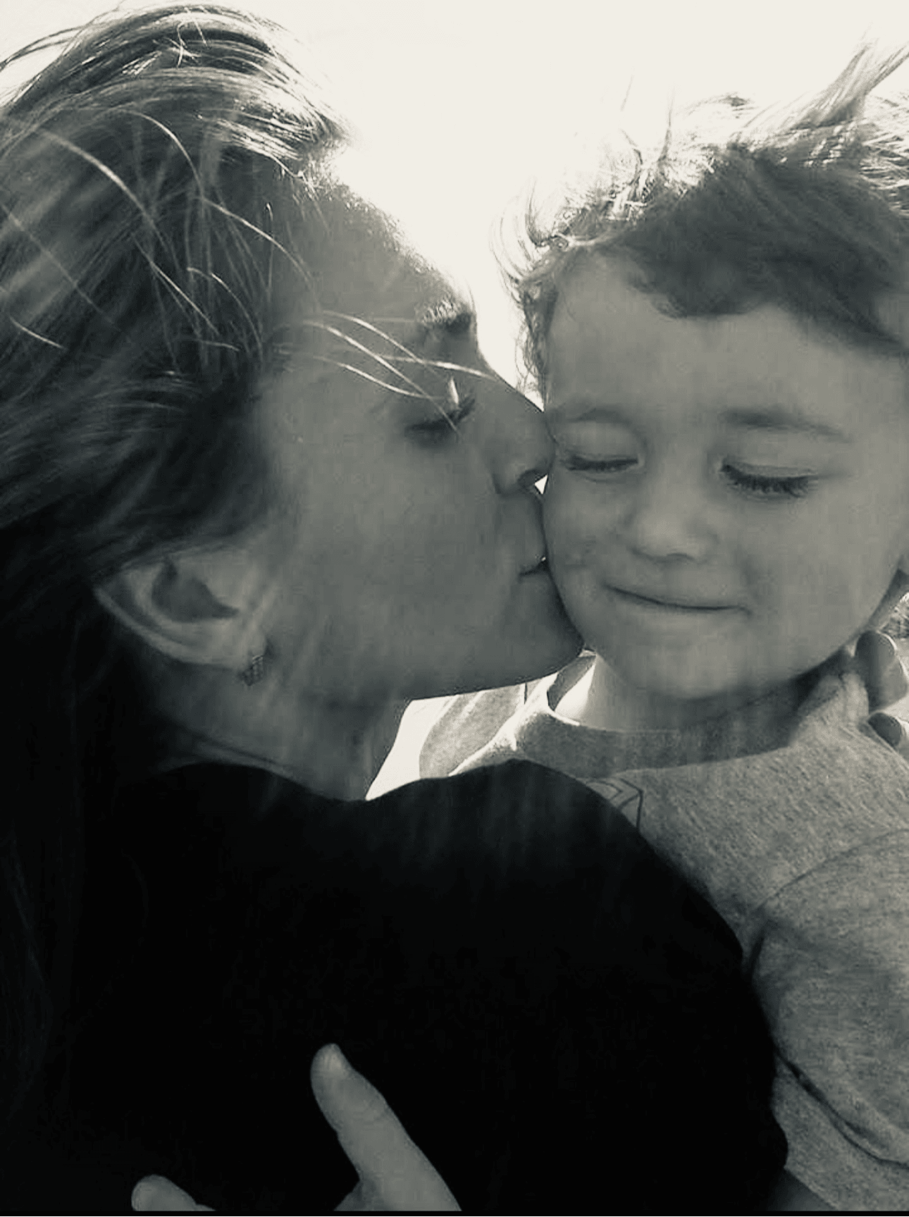 Woman kisses a child's cheek, both with closed eyes, in black and white.