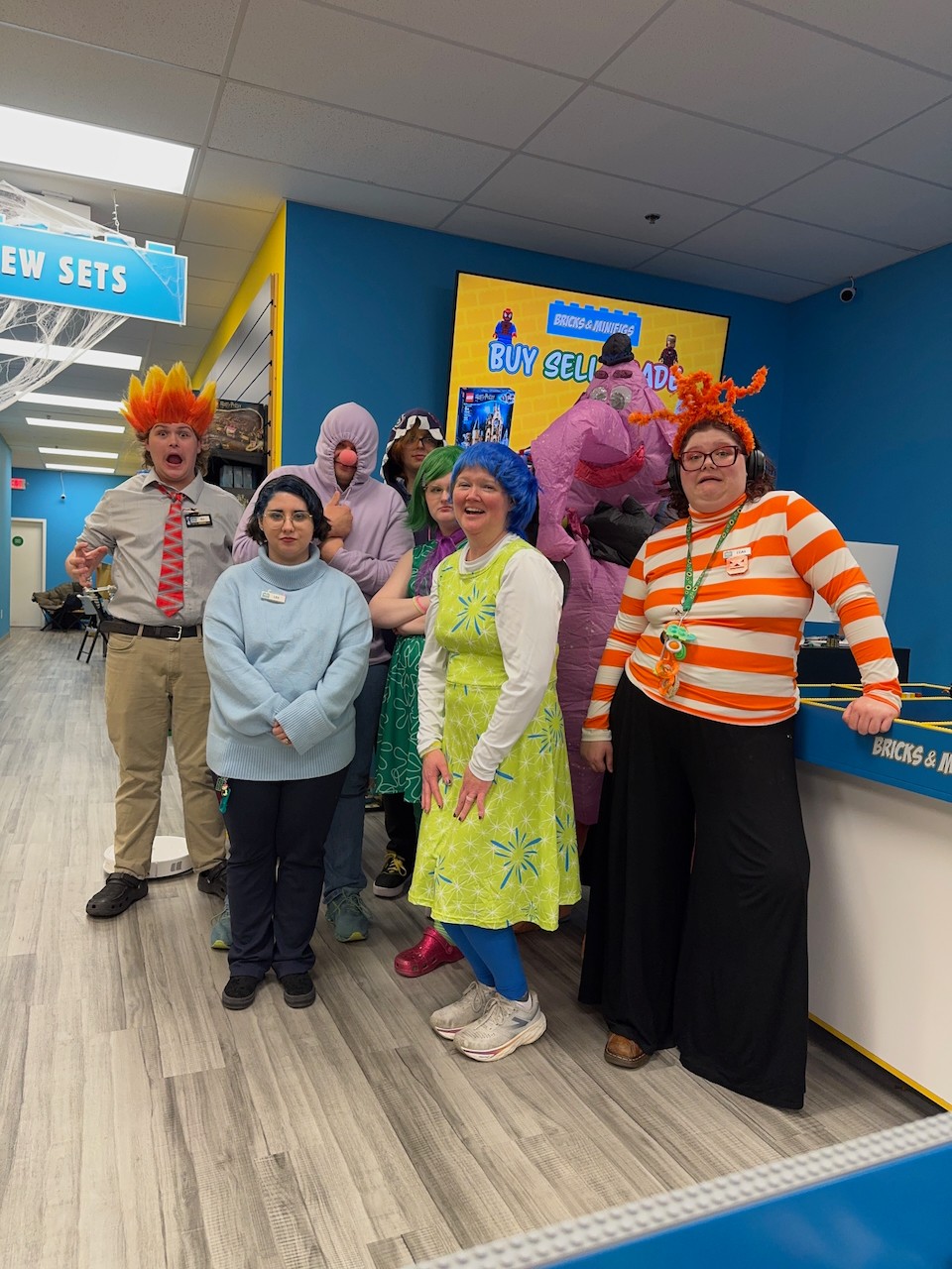 Group of people in colorful costumes and casual clothing standing inside a store with bright blue walls and a sign.