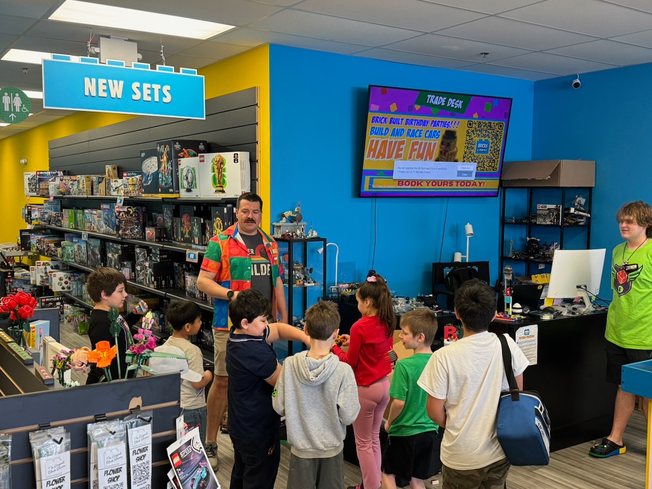 People shopping in a store with shelves, a cashier, and a large screen displaying colorful text and images.