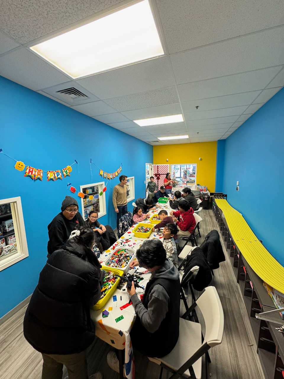 People gathered around a table with toys and activities in a colorful room with blue and yellow walls.