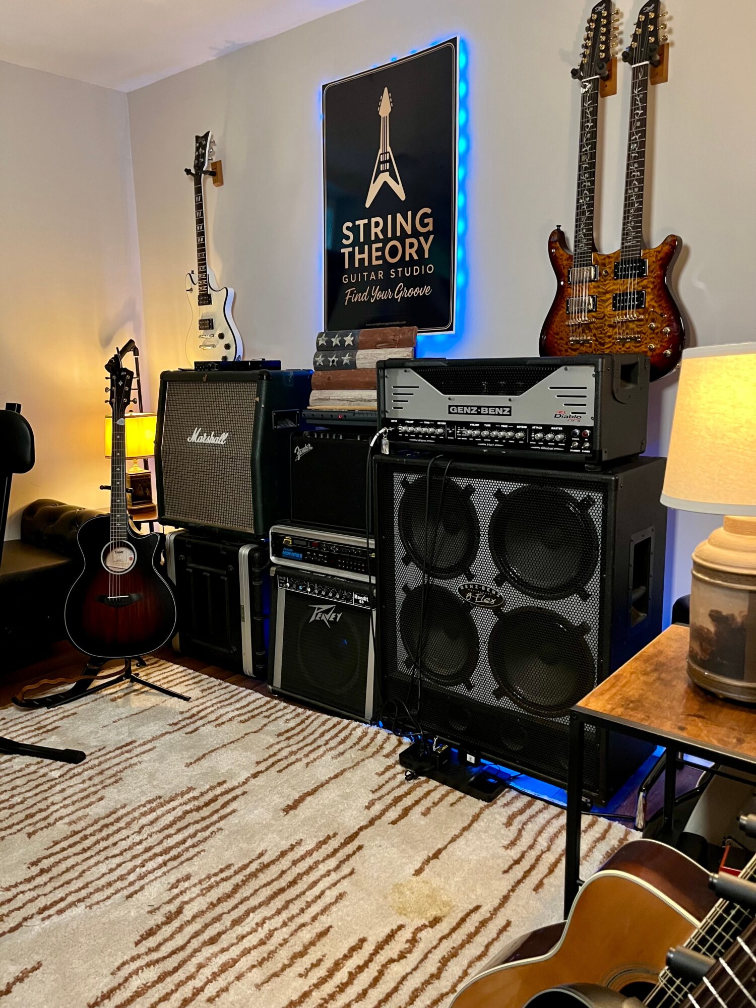 Music equipment including guitars, amplifiers, and speakers in a room with a 'String Theory' poster on the wall.