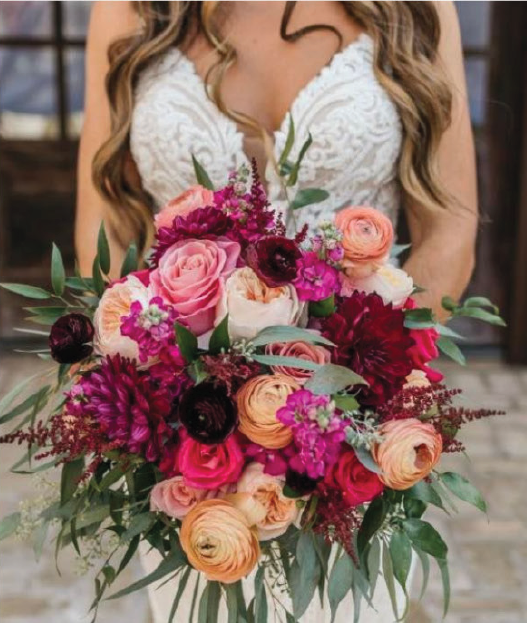 Woman in white lace dress holding a large colorful bouquet of roses, peonies, and greenery.