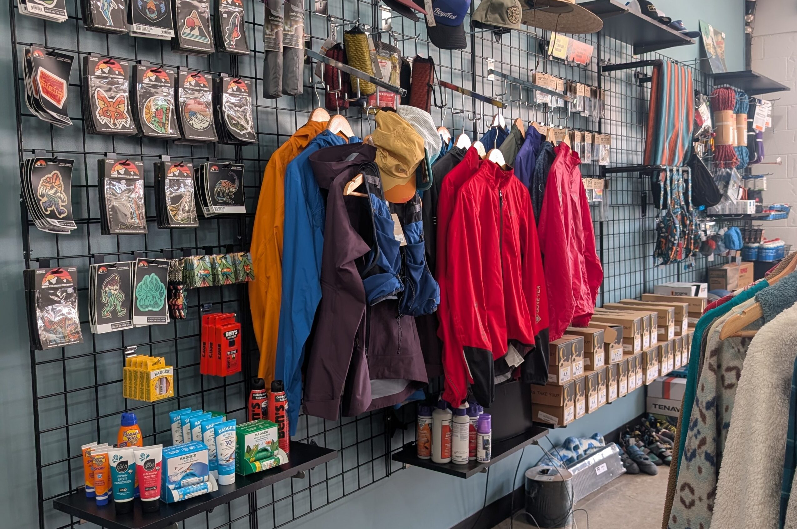 Clothing and accessories displayed on a store wall, including jackets, backpacks, and small items on shelves.